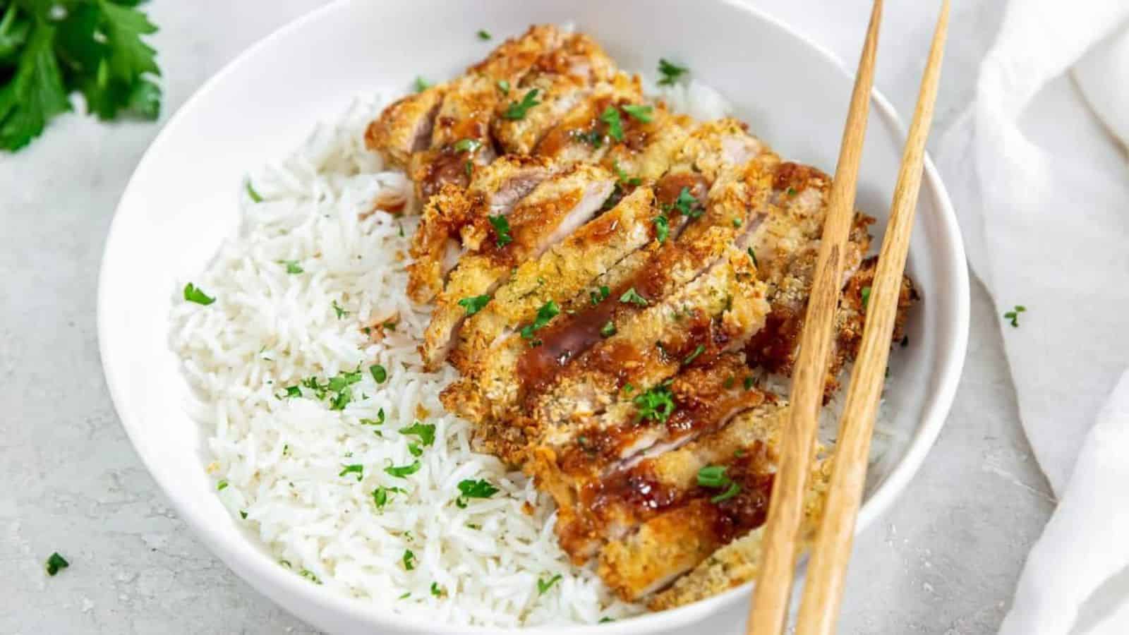 Air Fryer Chicken Katsu in a white bowl with a brown sauce, parsley, white rice, and chopsticks.