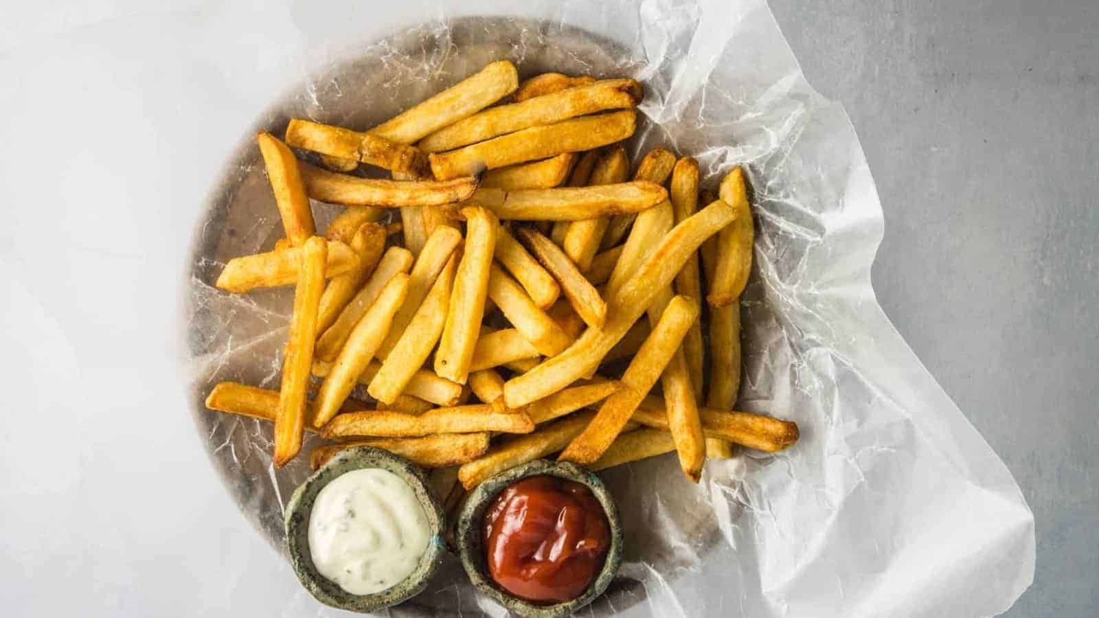 A plate of golden, crispy French fries is placed on white parchment paper.