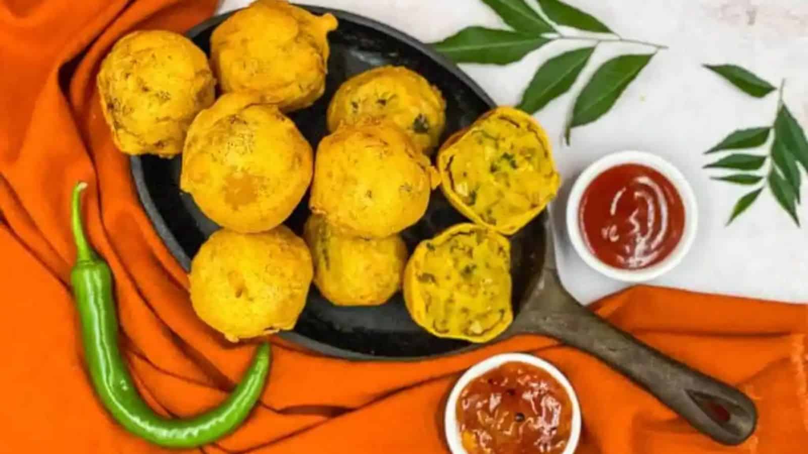 Overhead image of a pan full of aloo bonda with dips and green chili in the background.