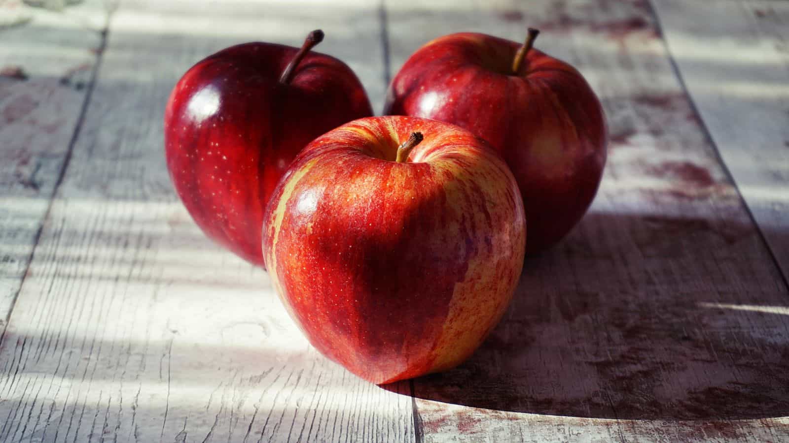 Three Red Apples on Wooden Surface.