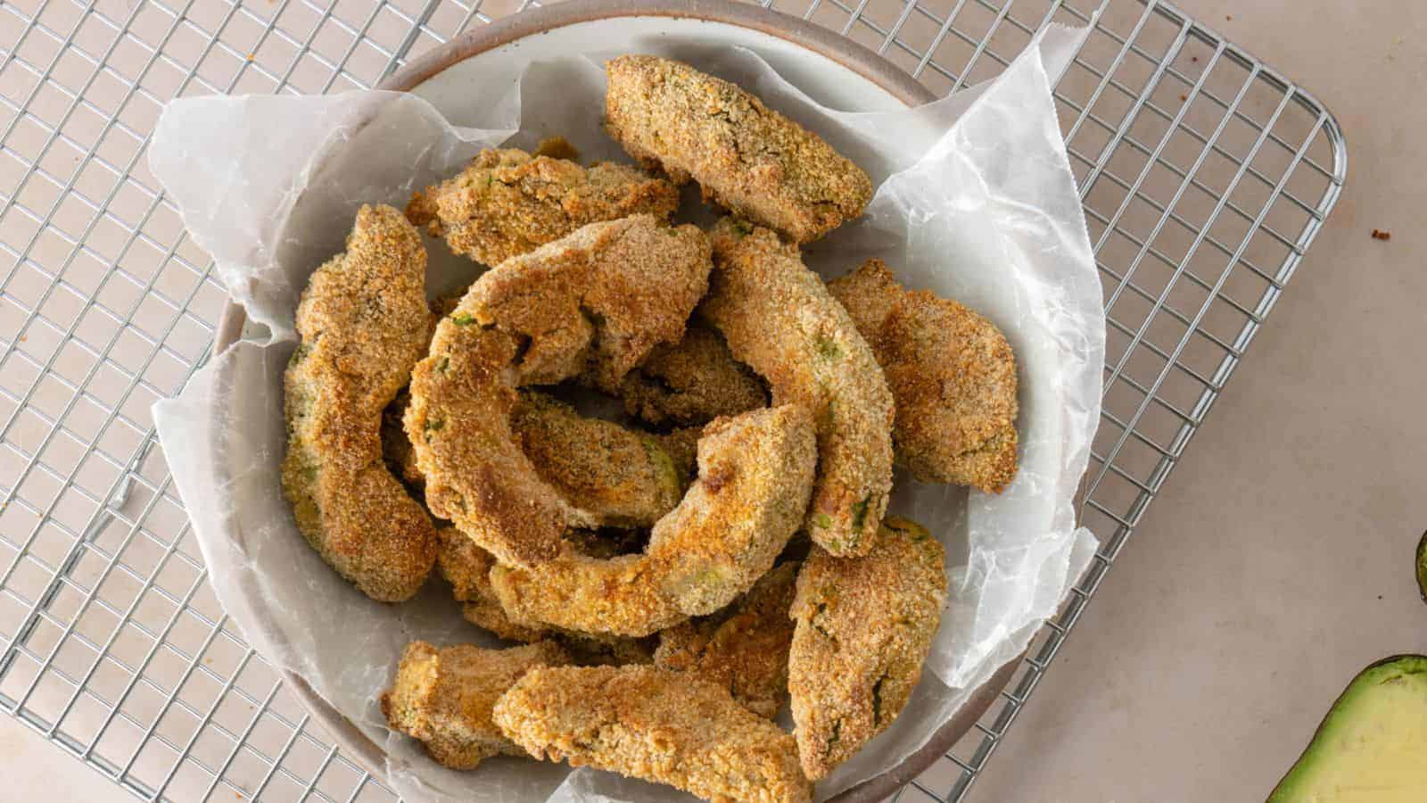 A top view image of a bowl of avocado fries laying on a cooling rack.