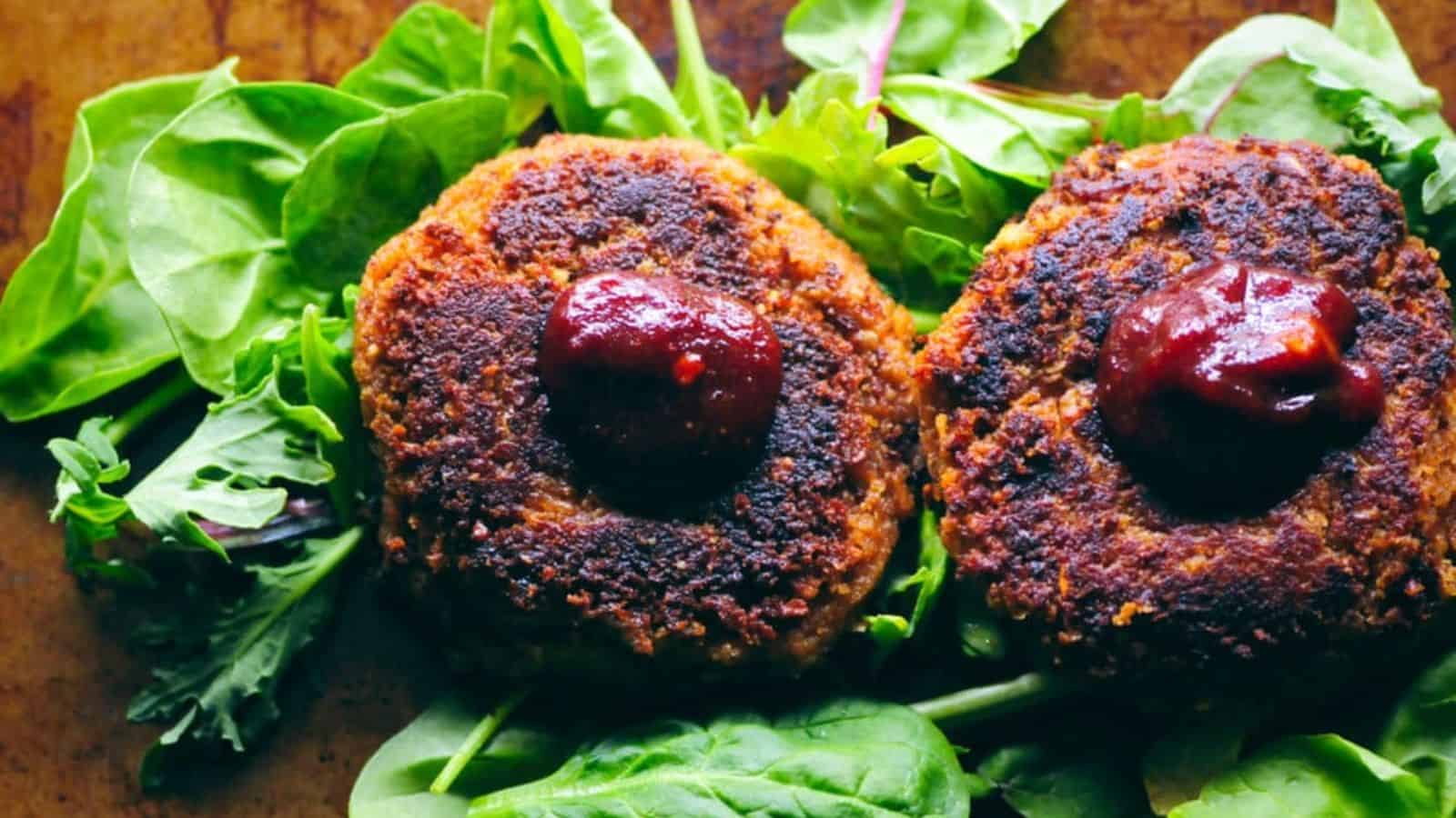 Overhead image of two BBQ walnut chickpea veggie burgers on a bed of green leafy vegetables.
