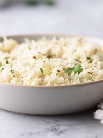 A straight view of cooked jeera rice in a white plate.