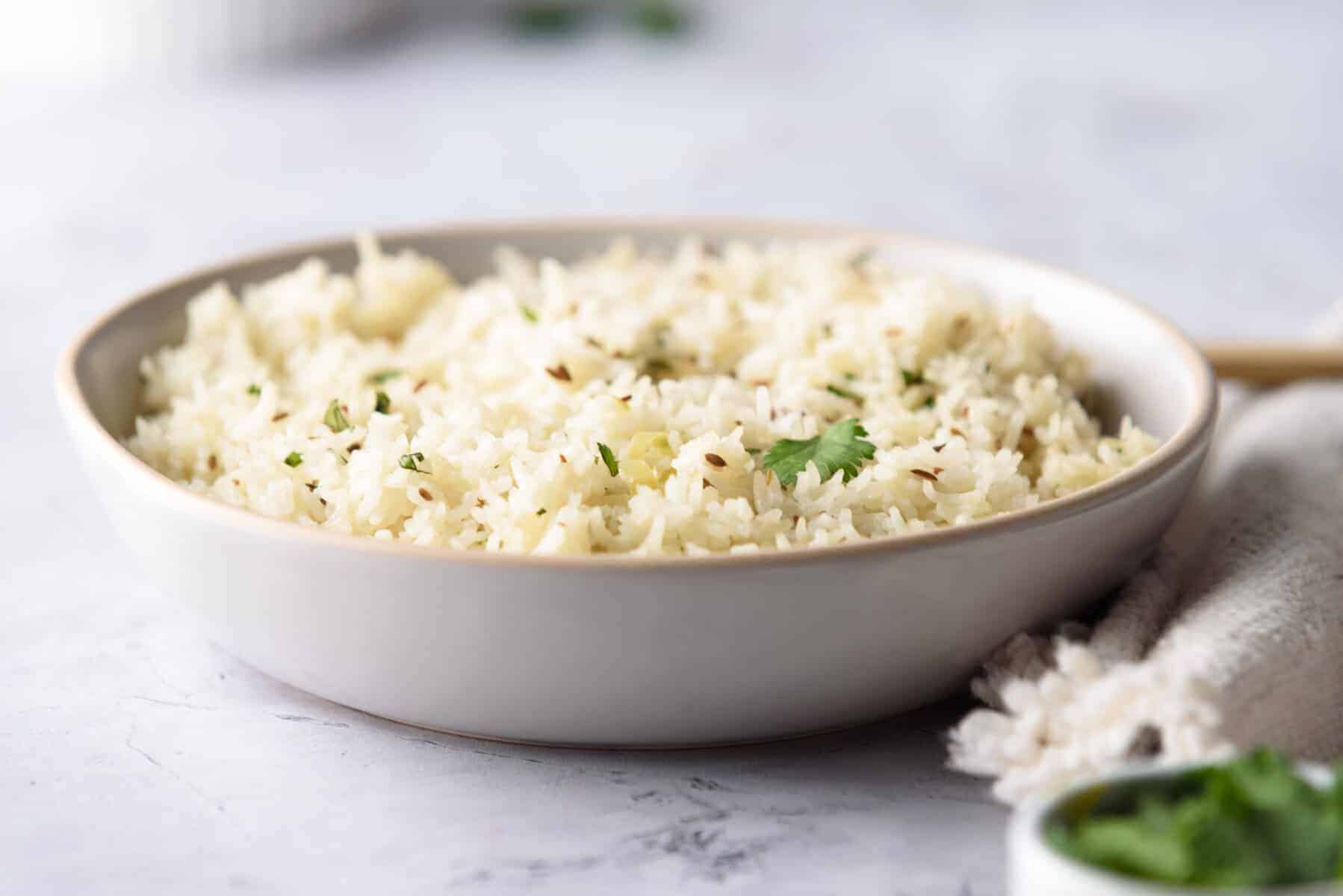 A straight view of cooked jeera rice in a white plate.