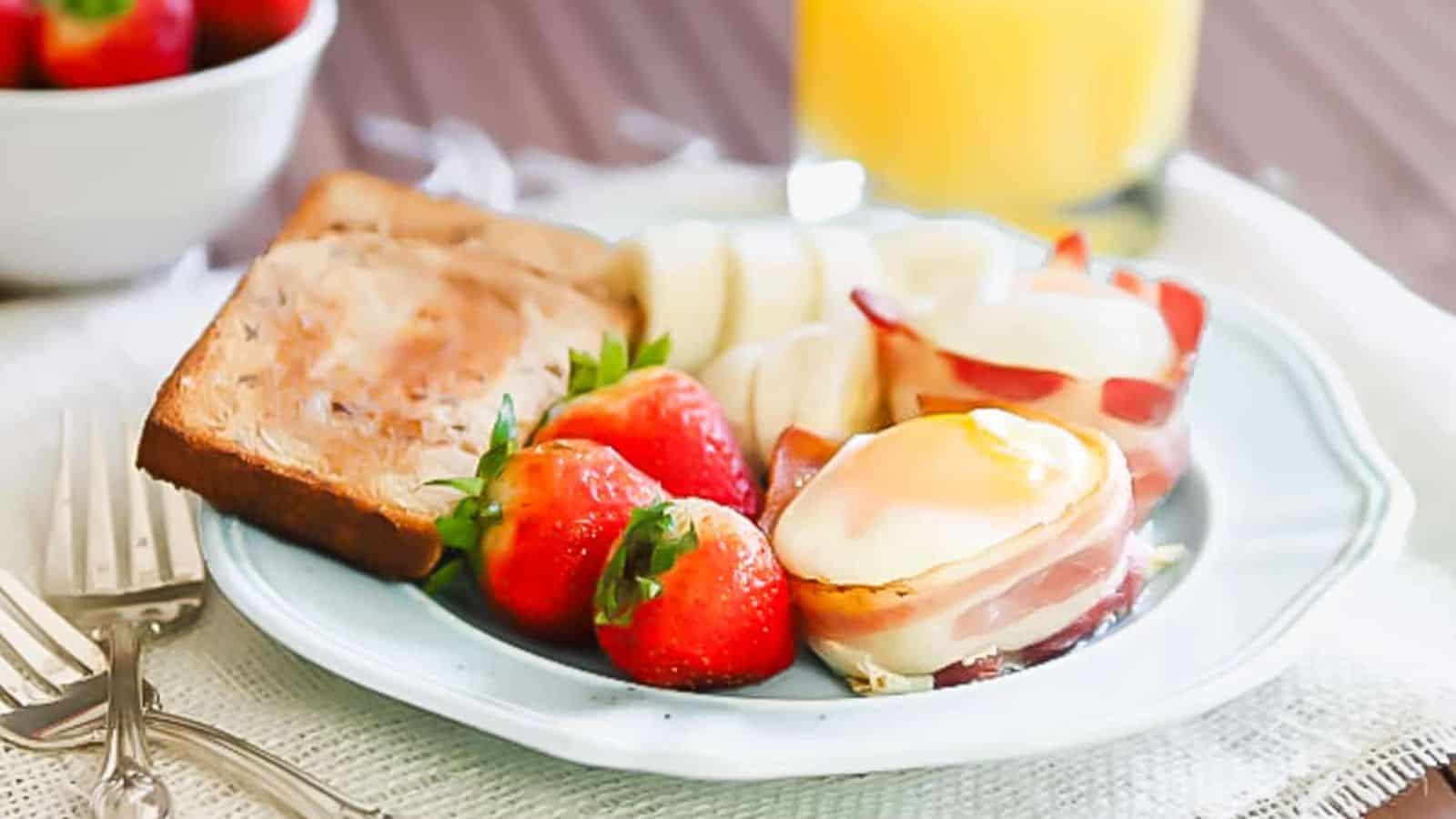 Bacon wrapped egg cups on a plate with toast and strawberries.