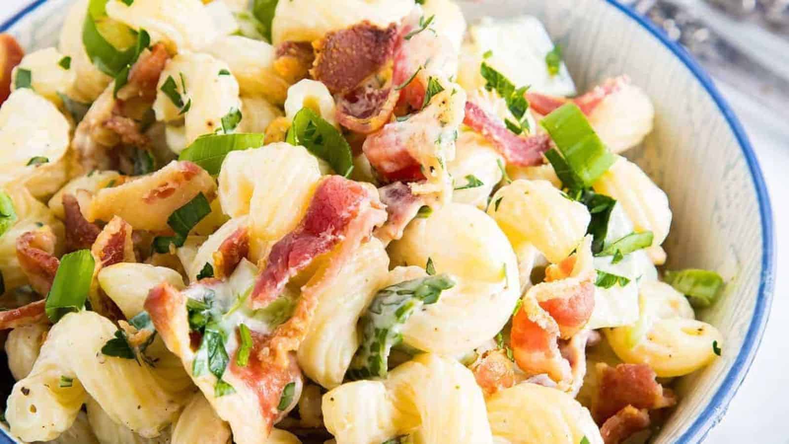 A close up image of pasta salad with bacon and green onions in a bowl.