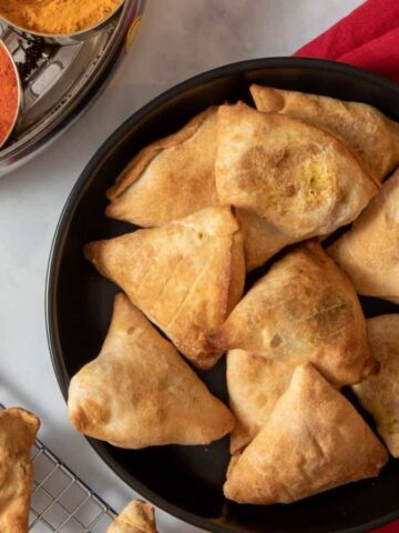 Top view image of healthy samosas on a black plate with additional samosas on a cooling rack.