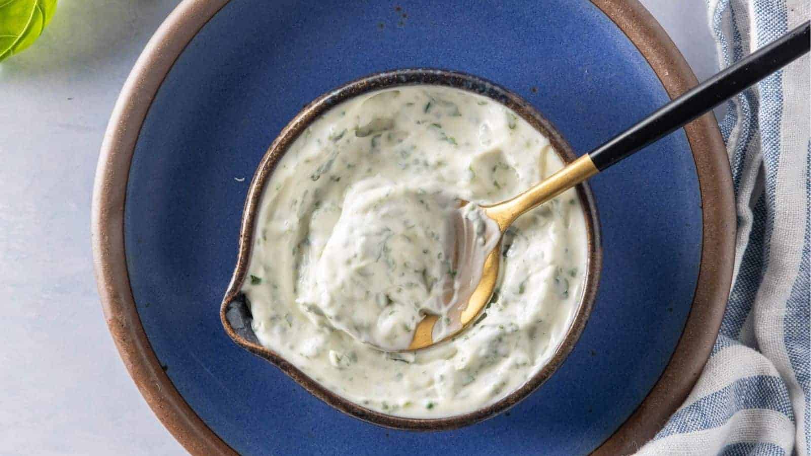 A top-down view of a small bowl filled with basil mayonnaise on a blue plate.