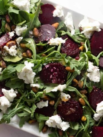 Close up of beet salad on a white platter with two forks on the right side.