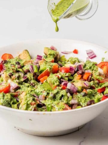 Mediterranean Black Bean Salad in a white bowl being drizzled with cilantro lime dressing.