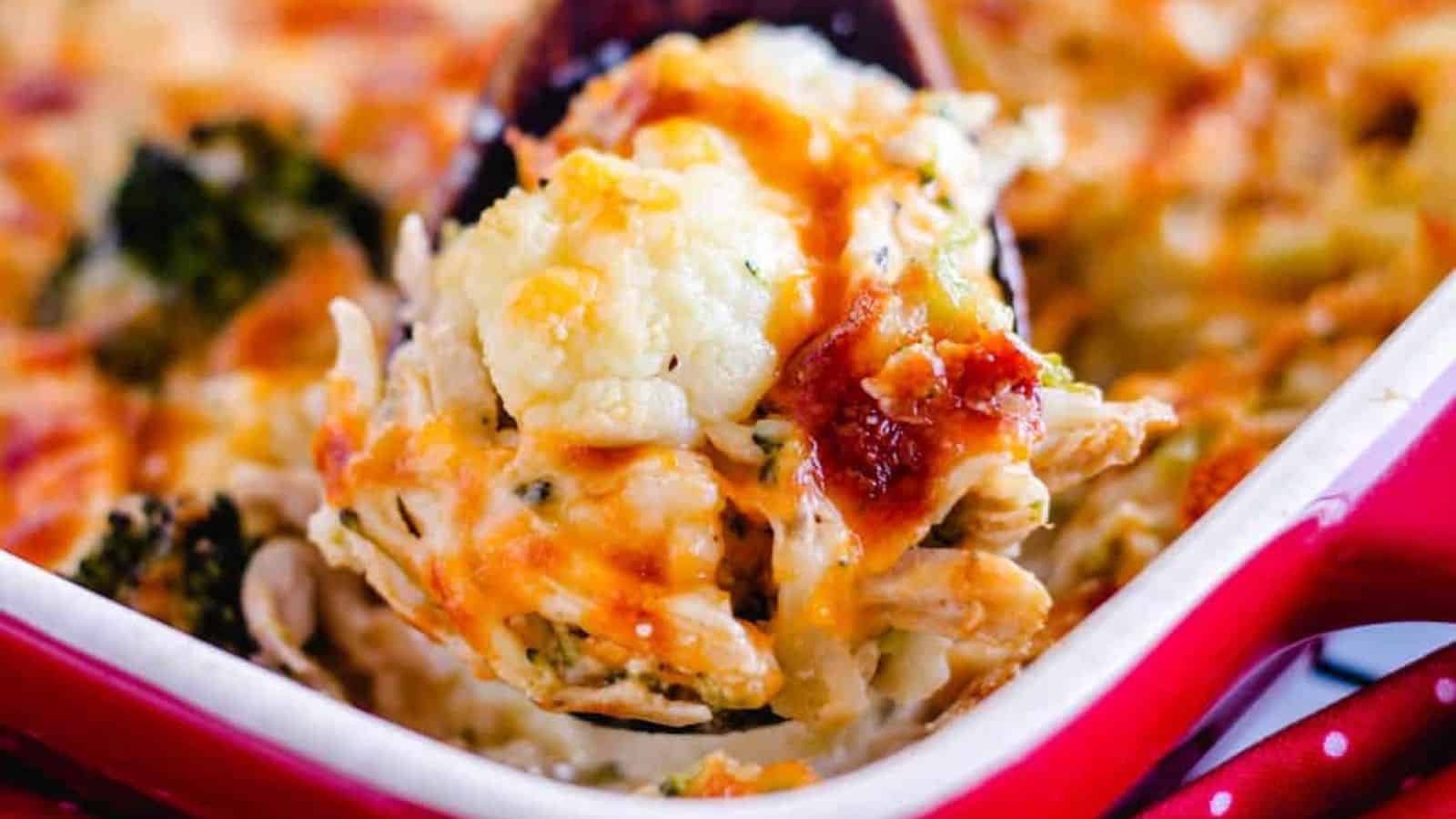 A wooden spoon scooping out a portion of cauliflower chicken casserole.