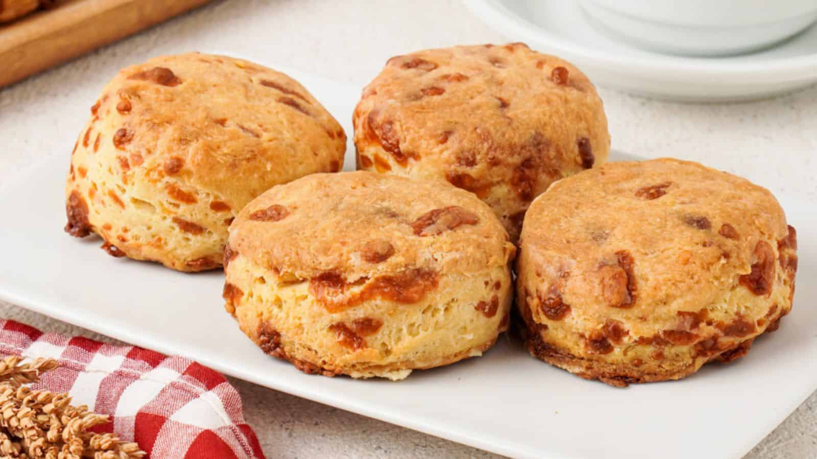 Close-up of four flaky buttermilk cheddar cheese biscuits arranged on a white plate.