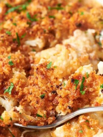 Cheesy cauliflower casserole in a white dish with spoons.