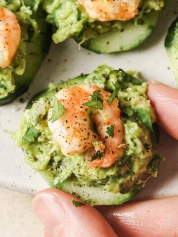 A person holding a cucumber with shrimp and guacamole.