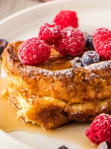 A close up image of croissant French toast topped with blueberries and raspberries.