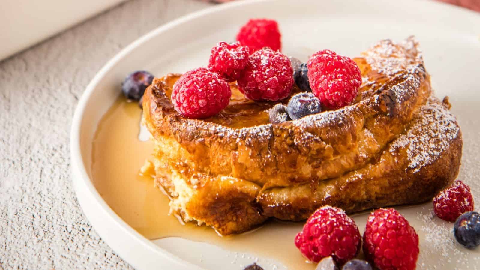 A close up image of croissant French toast topped with blueberries and raspberries.