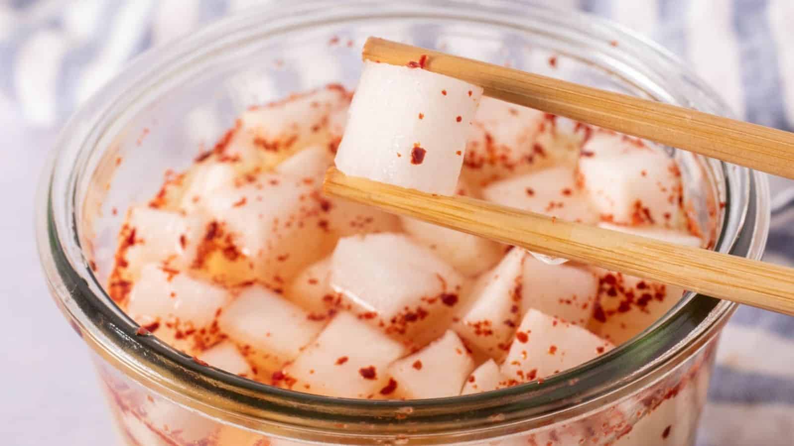 A close-up of a glass jar filled with small, cubed pieces of radish, seasoned with red chili flakes.