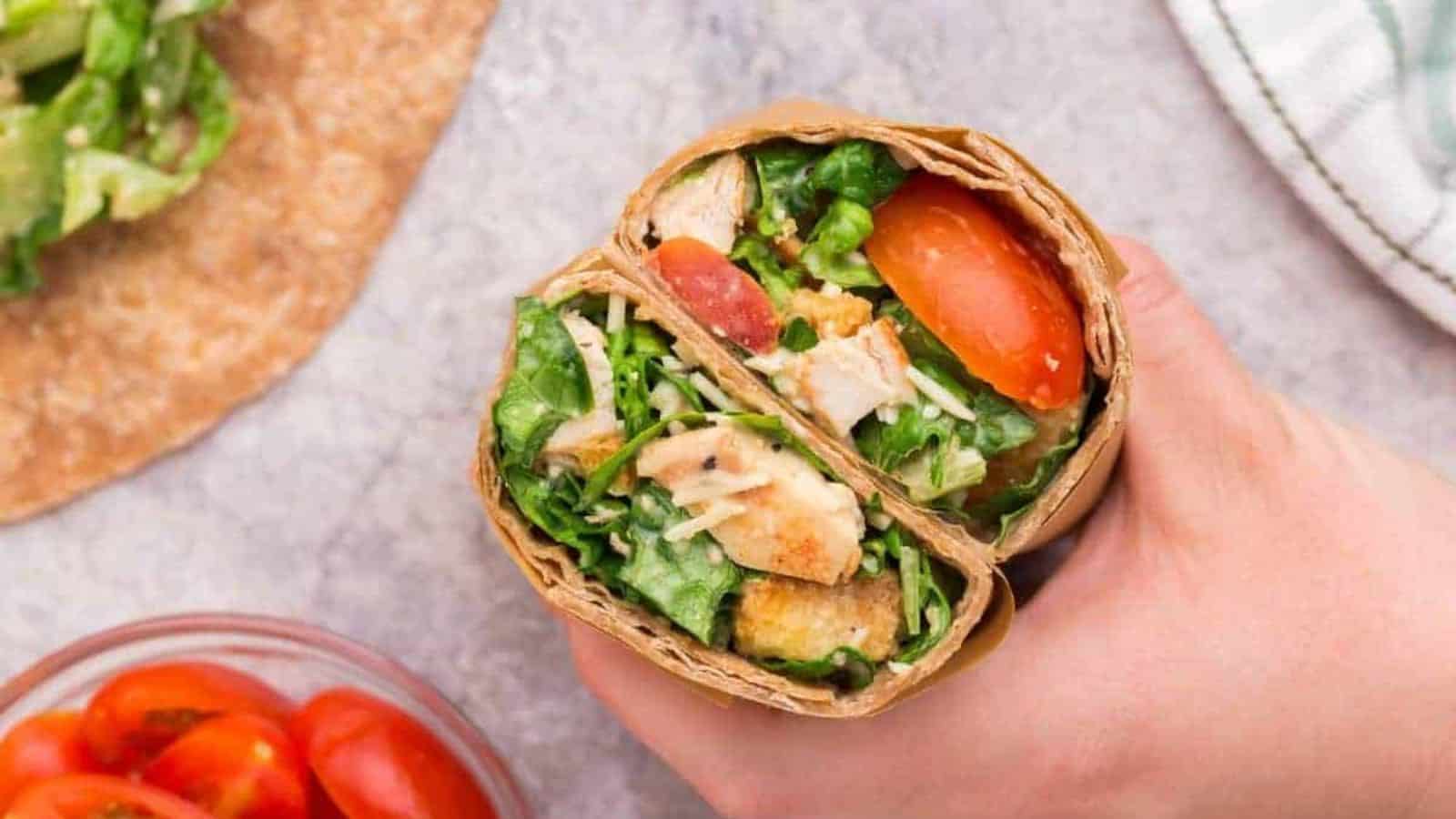 A hand holding a sliced Easy Chicken Caesar Wrap.