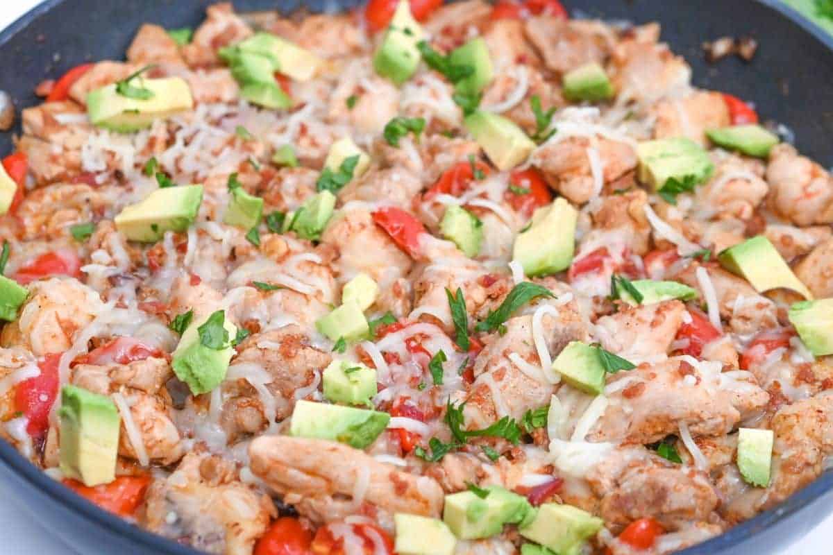 Cooked chicken skillet, with cheese, pepper, avocado and cilantro on it.