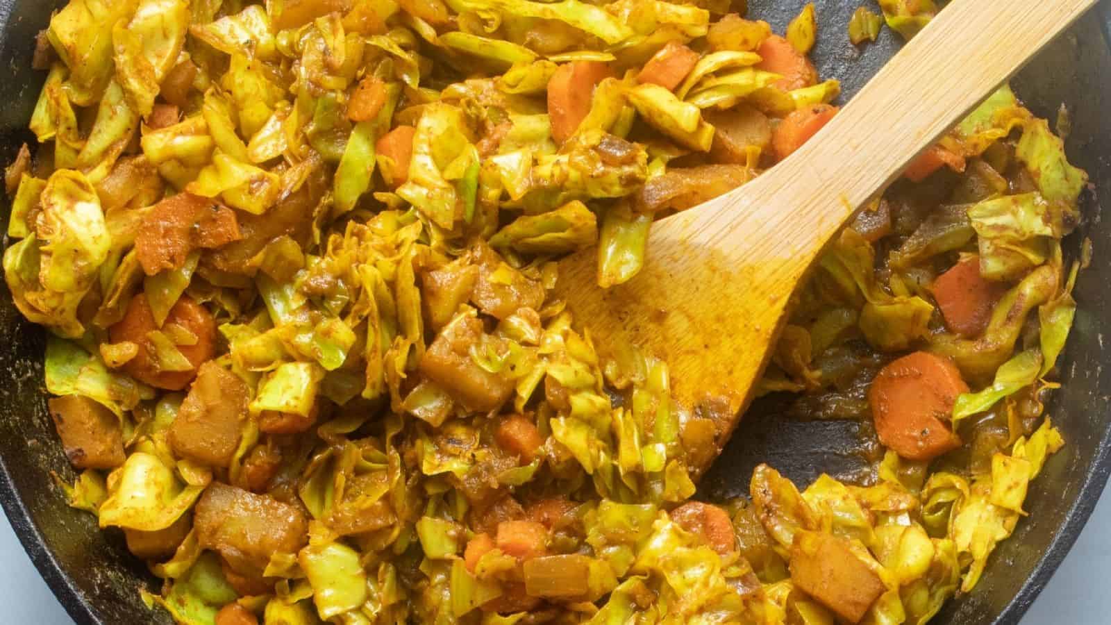 A close up image of cooked Ethiopian cabbage in a skillet pan with a wooden serving spoon mixing the dish.