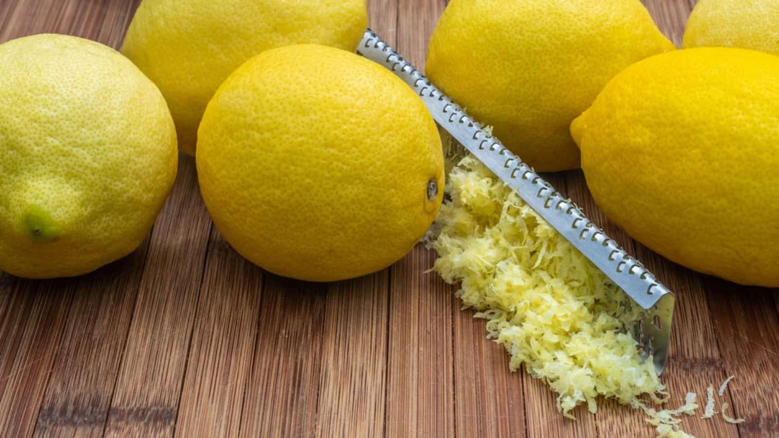 Ripe lemons with zest and grater on table.
