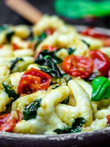 Brown plate with gnocci, tomatoes and basil leaves.