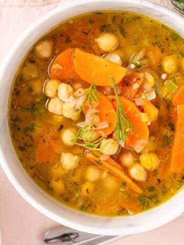 An image of greek chickpea soup in a bowl with utensils beside it.