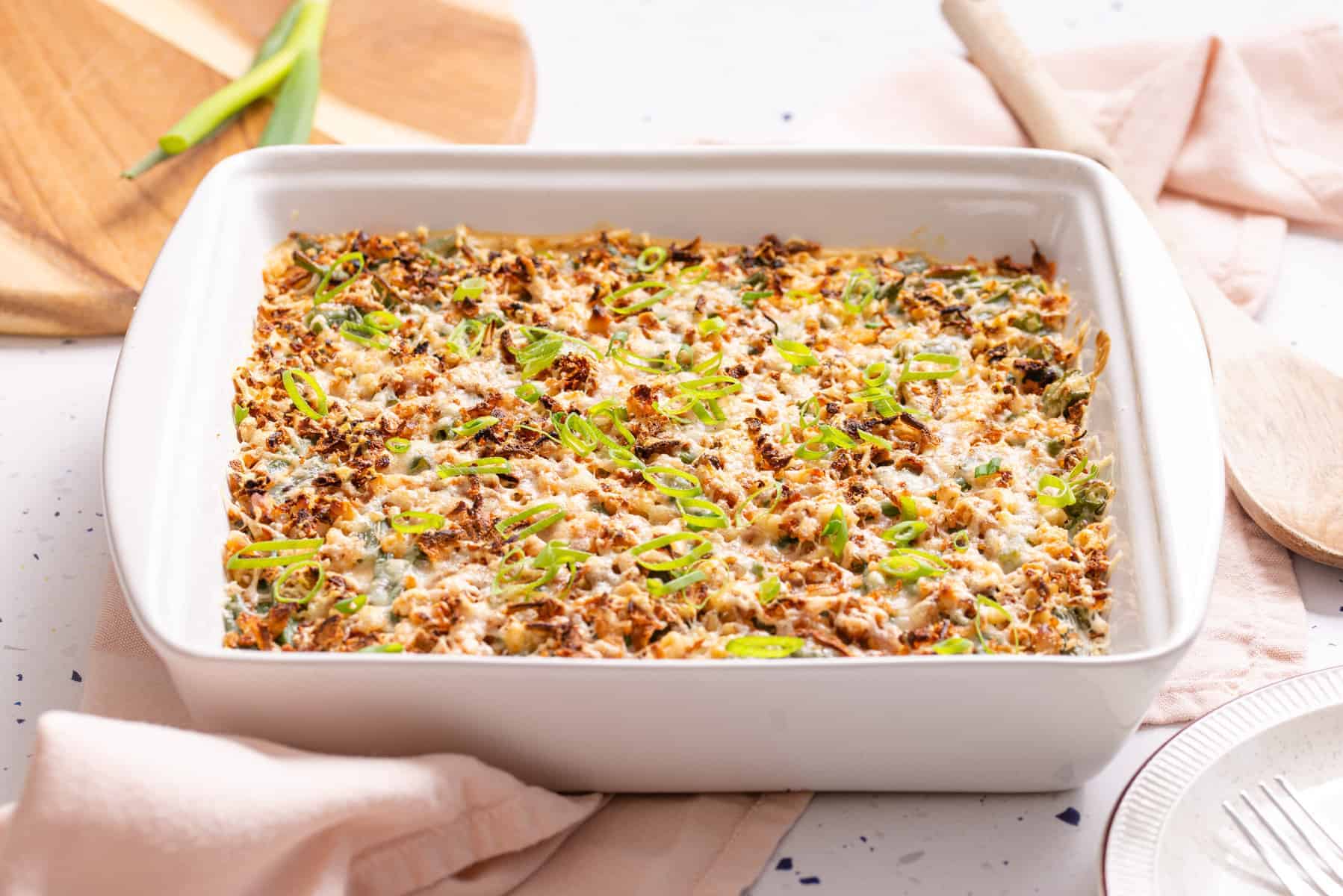 A  Green Bean Casserole with Cream Cheese topped with a golden-brown crust and garnished with sliced green onions.