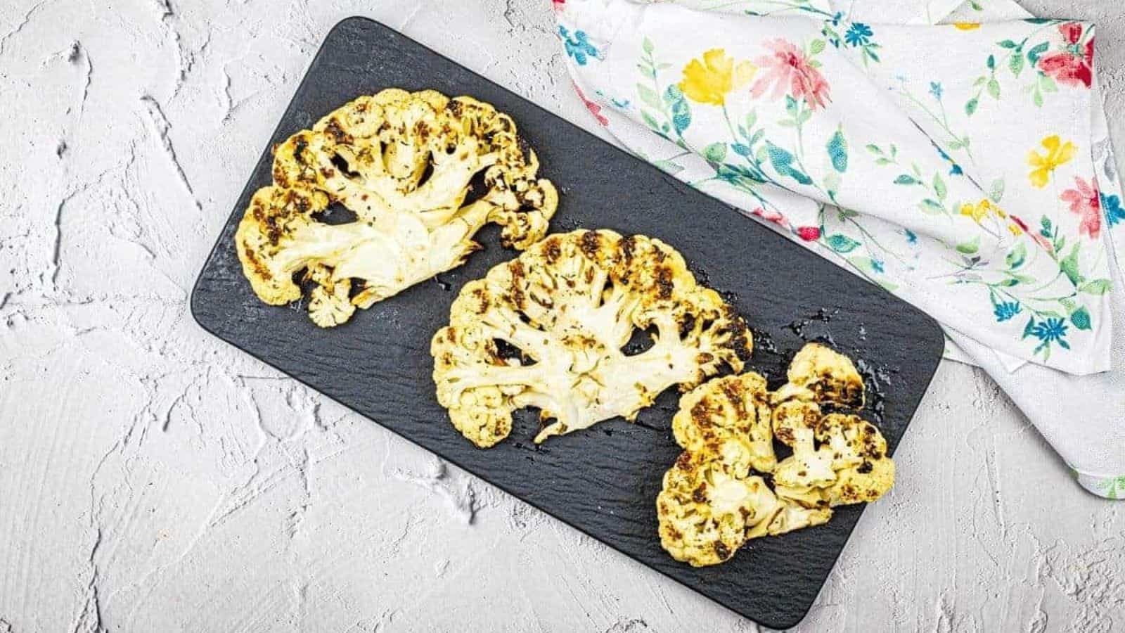 Three pieces of grilled cauliflower steaks on a black plate.