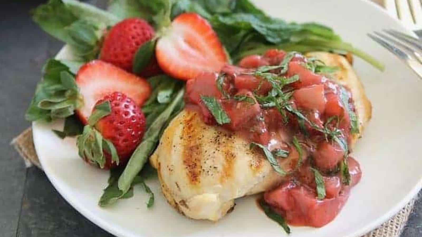 Grilled chicken on a plate with strawberry basil sauce, fresh cut strawberries and greens.