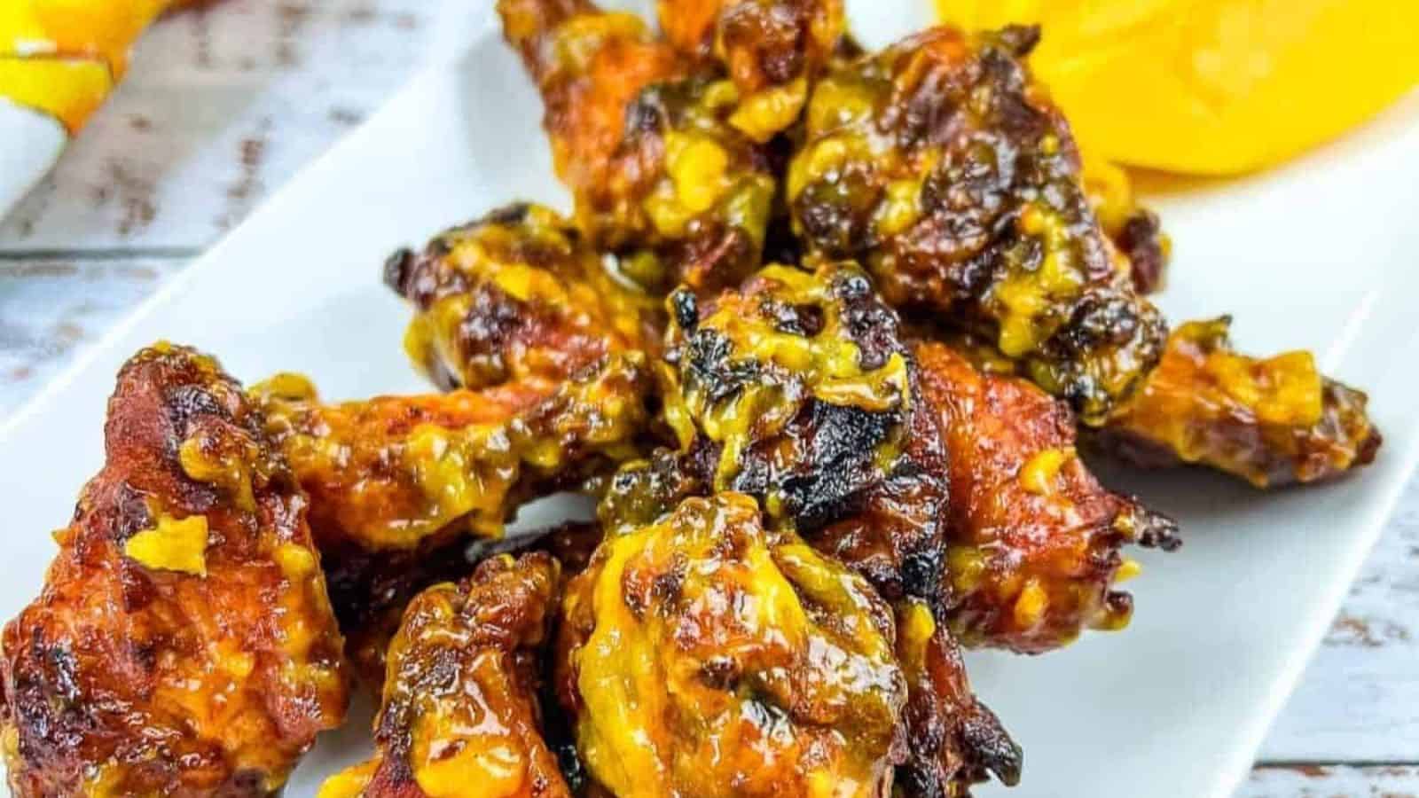 A plate of chicken wings on a white plate with a slice of mango.