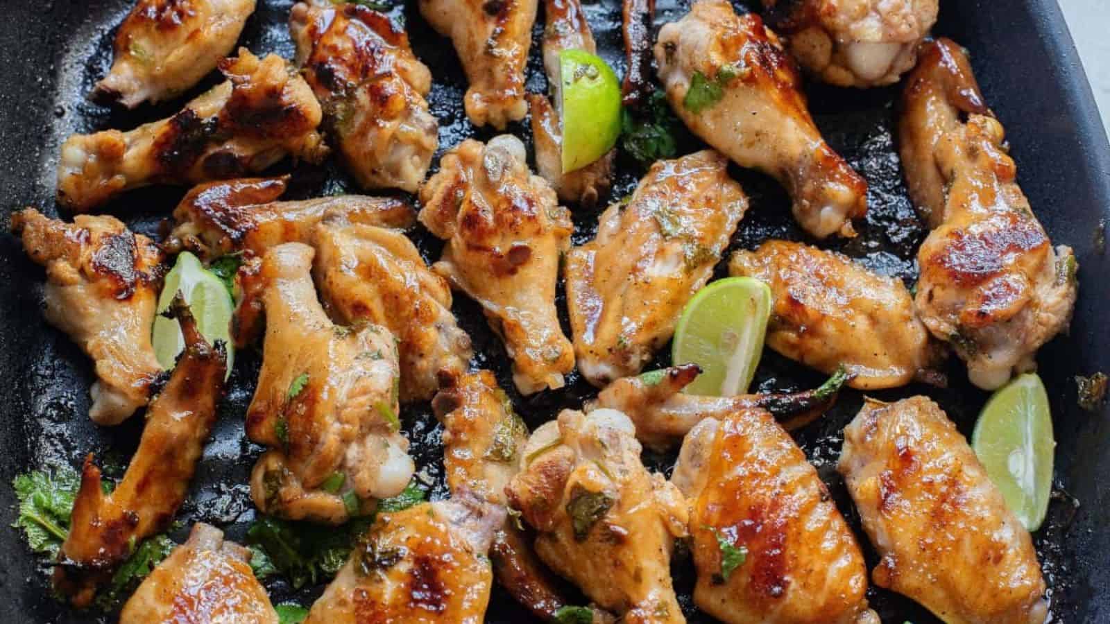 Gluten-free chicken wings in honey garlic sauce on a grill pan with cilantro and lime on them.