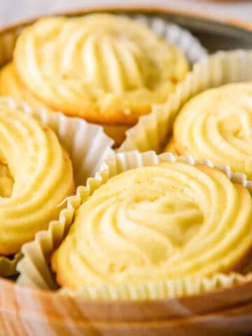 Four swirled butter cookies, each nestled in a white paper liner, arranged on a wooden tray.