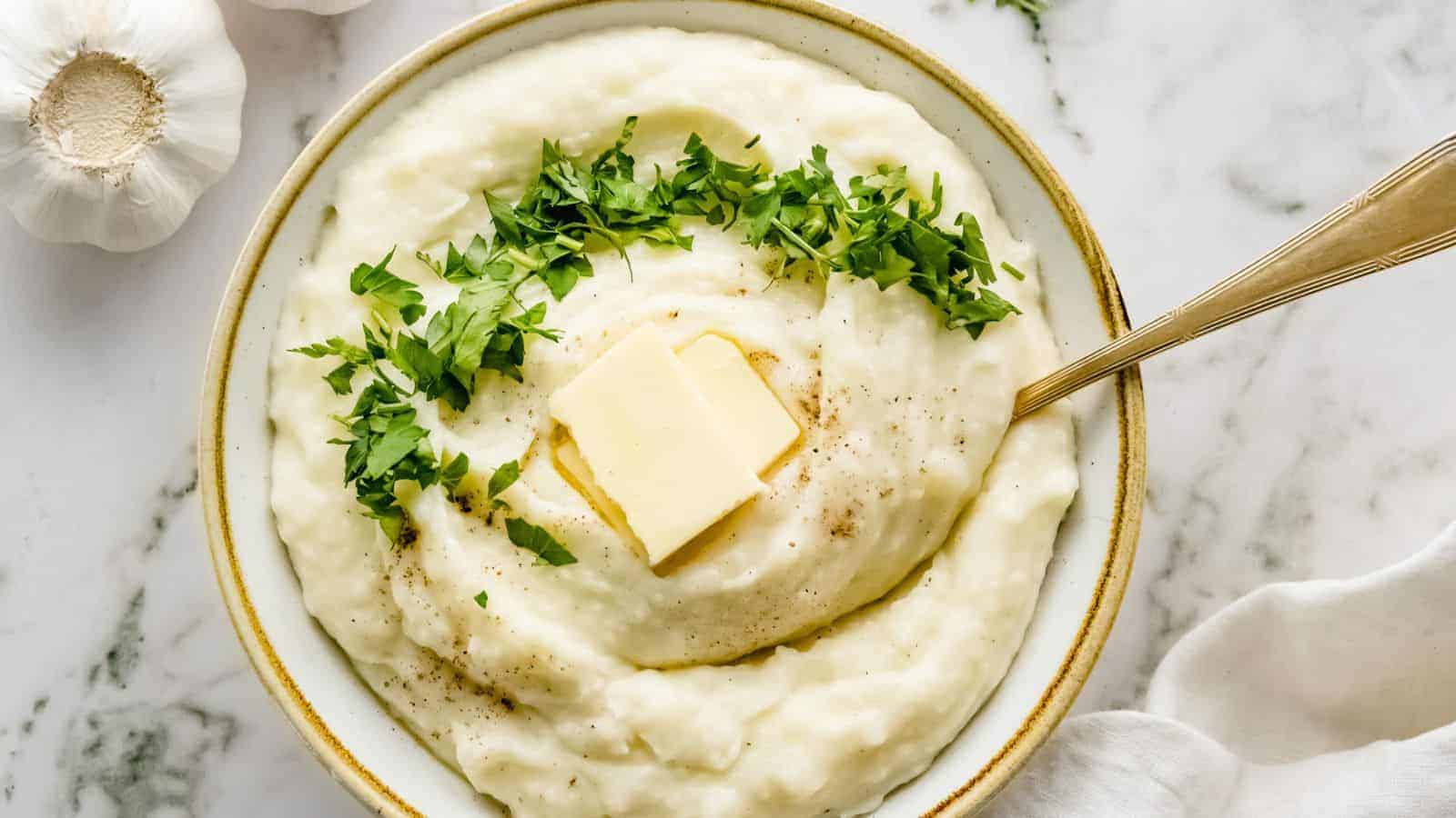 Close up of mashed potatoes with a slice of butter and a golden spoon.