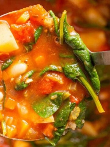 A close-up image of a ladle filled with Instant Pot minestrone soup, with the pot in the background.