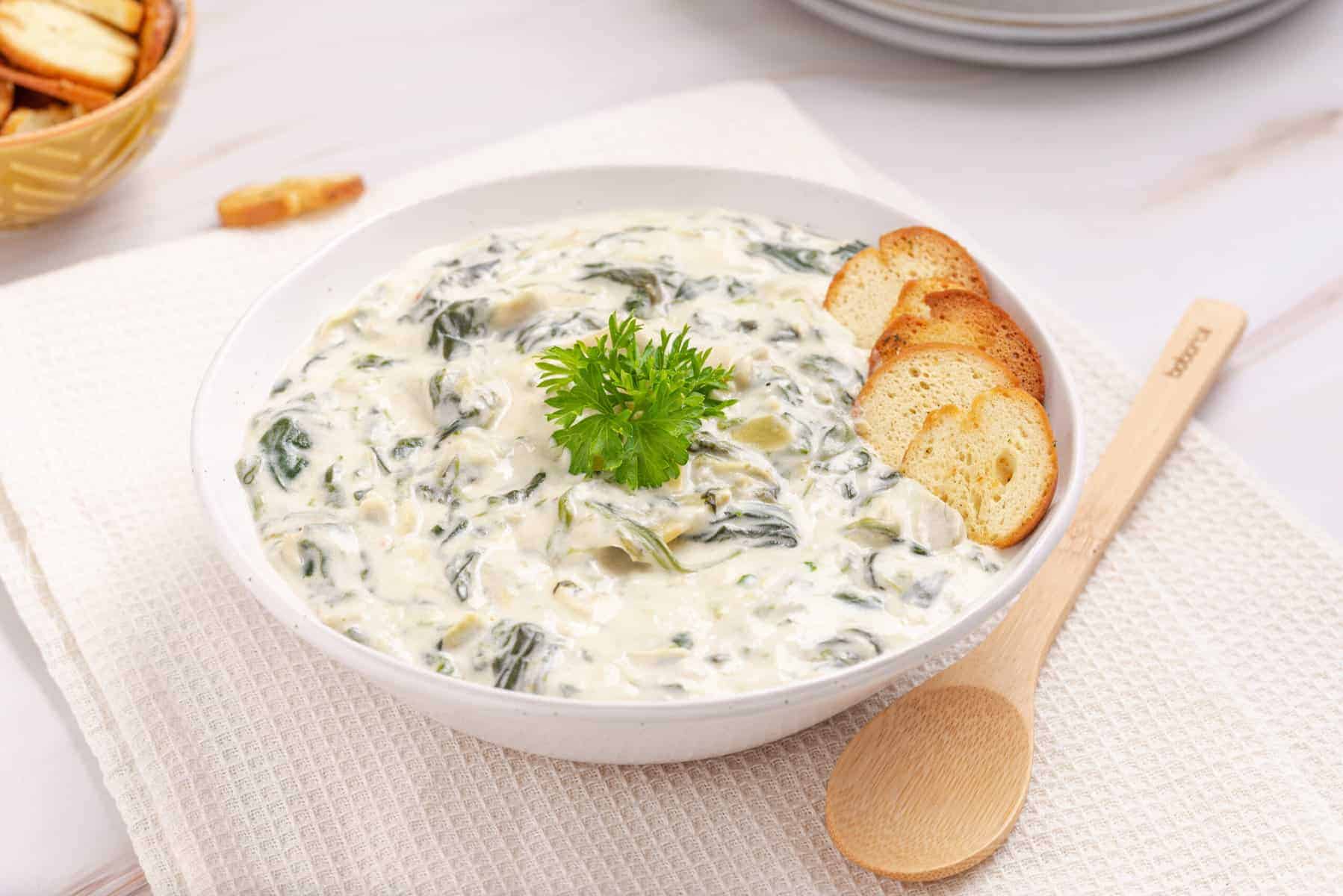 A close up photo of instant pot spinach artichoke dip placed in a white bowl with wooden spoon in the side.