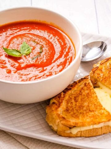 Close up of Instant Pot Tomato soup in a white bowl, with grilled cheese next to it.