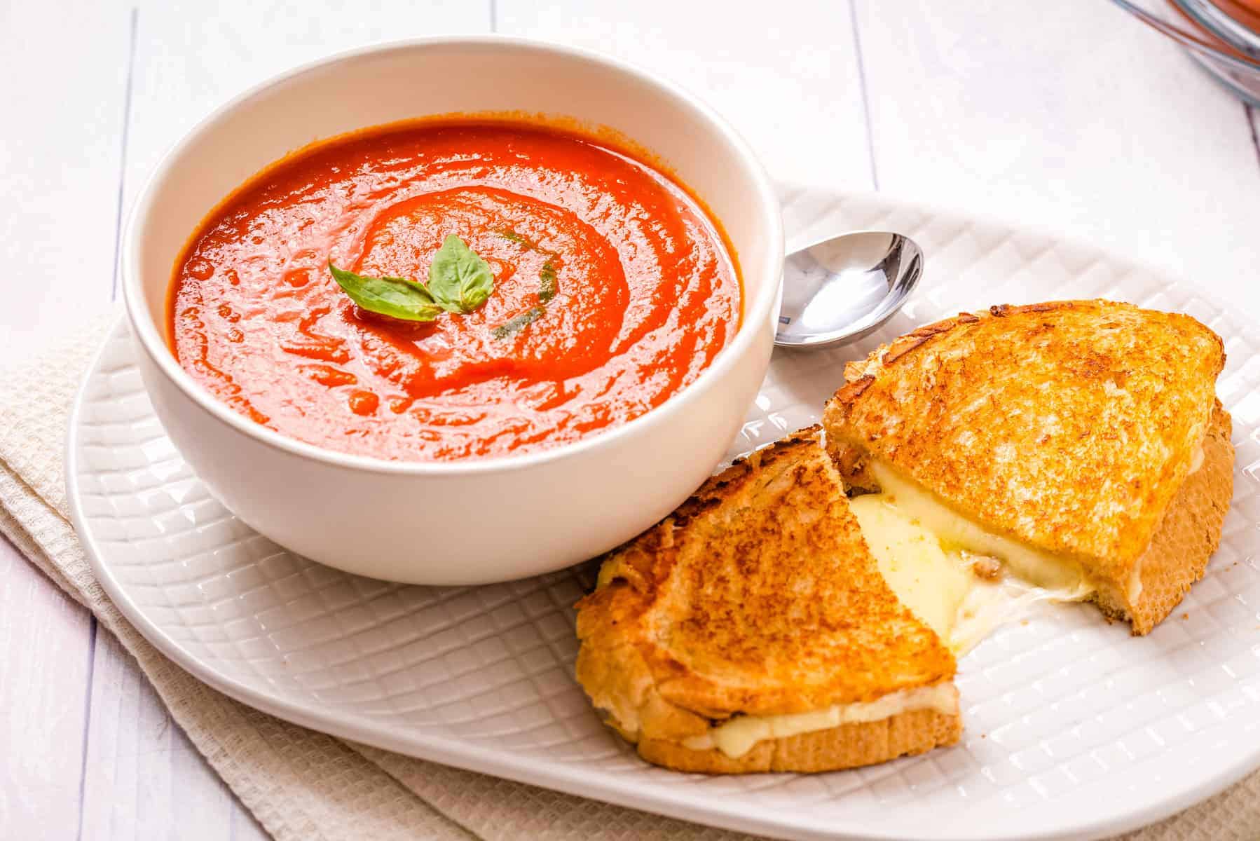 Close up of Instant Pot Tomato soup in a white bowl, with grilled cheese next to it.