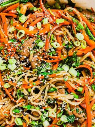 Overhead view of Korean sweet potato glass noodles in a white pan with chopsticks and garnish in the background.