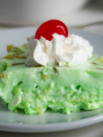 Piece of lime jello salad topped with whipped cream and a cherry.