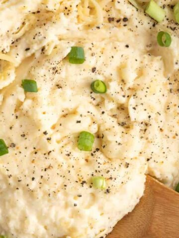 Close up of mashed potatoes in a Dutch oven, with wooden spoon.