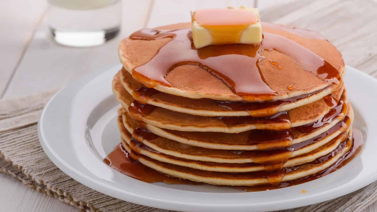 Stack of pancakes with syrup and butter in a white plate.