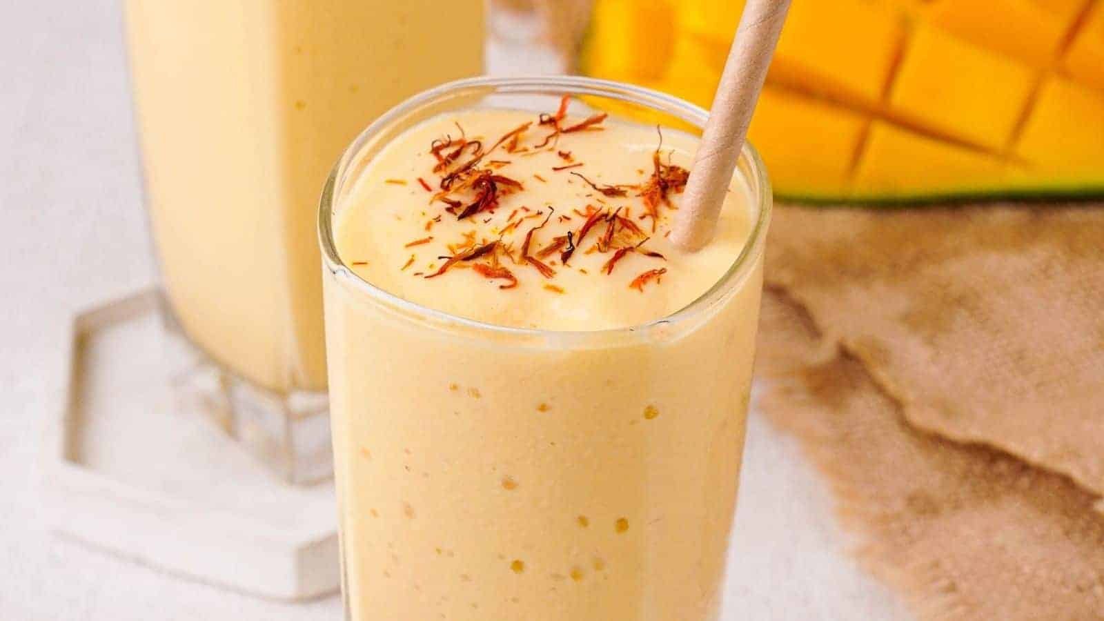 A close up image of mango lassi in a glass with straw.