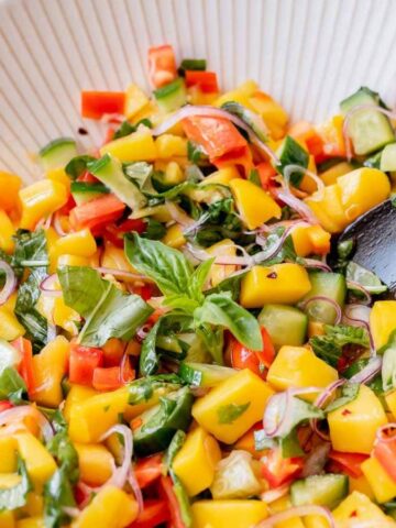 Close-up image of mango salad with a wooden spoon in a white bowl.