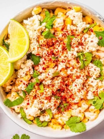 An overhead image of Mexican street corn salad in a bowl with two slices of lime resting on the side.