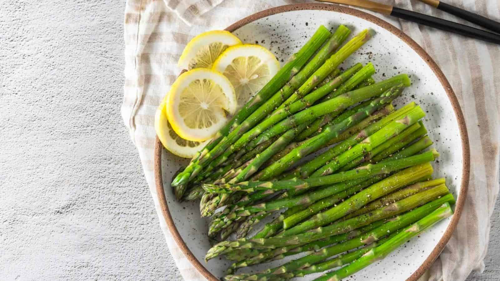 An overhead image of microwave asparagus in a serving plate with slices of lemon on the side.