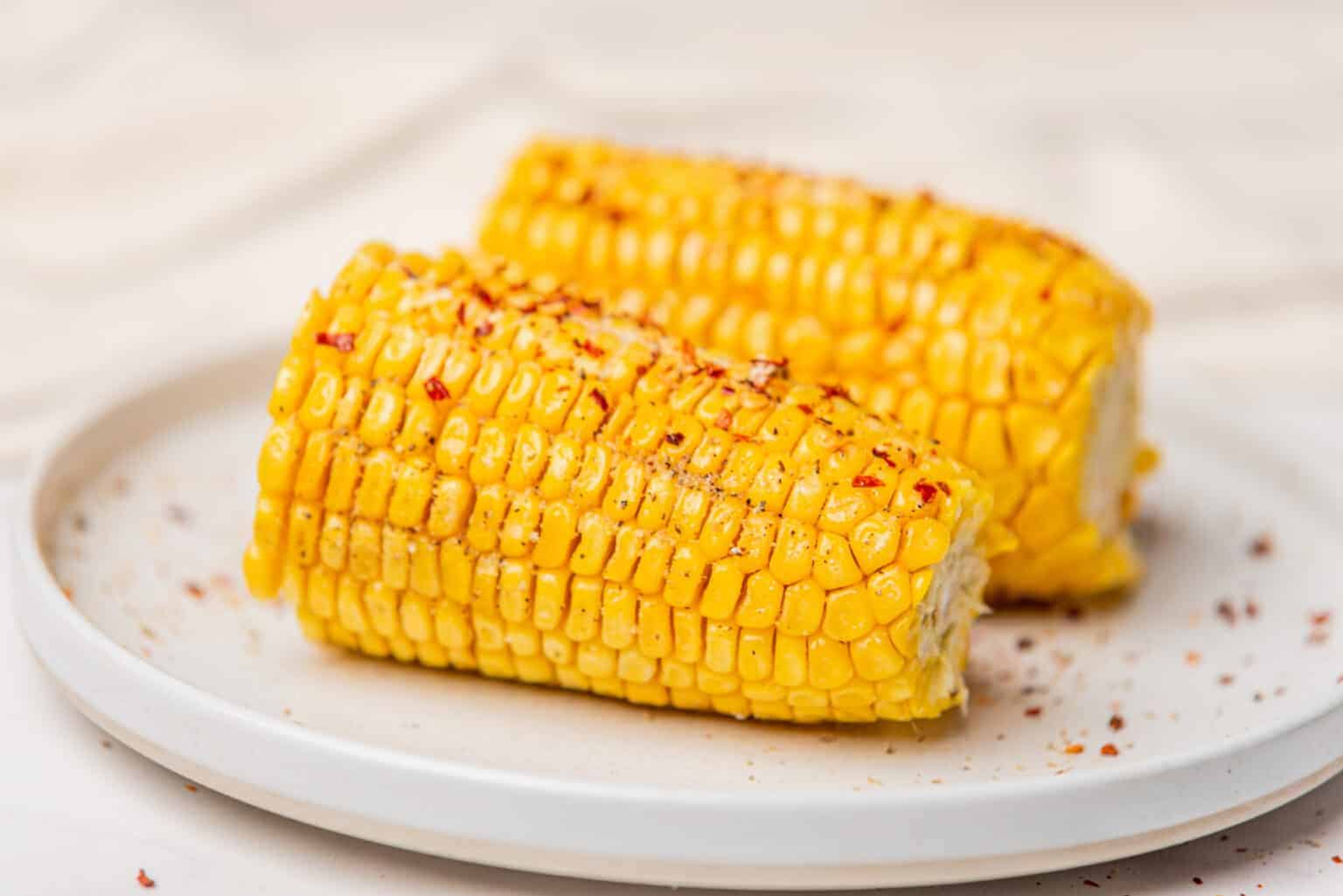 An image of a halved corn on a plate topped with chili flakes.