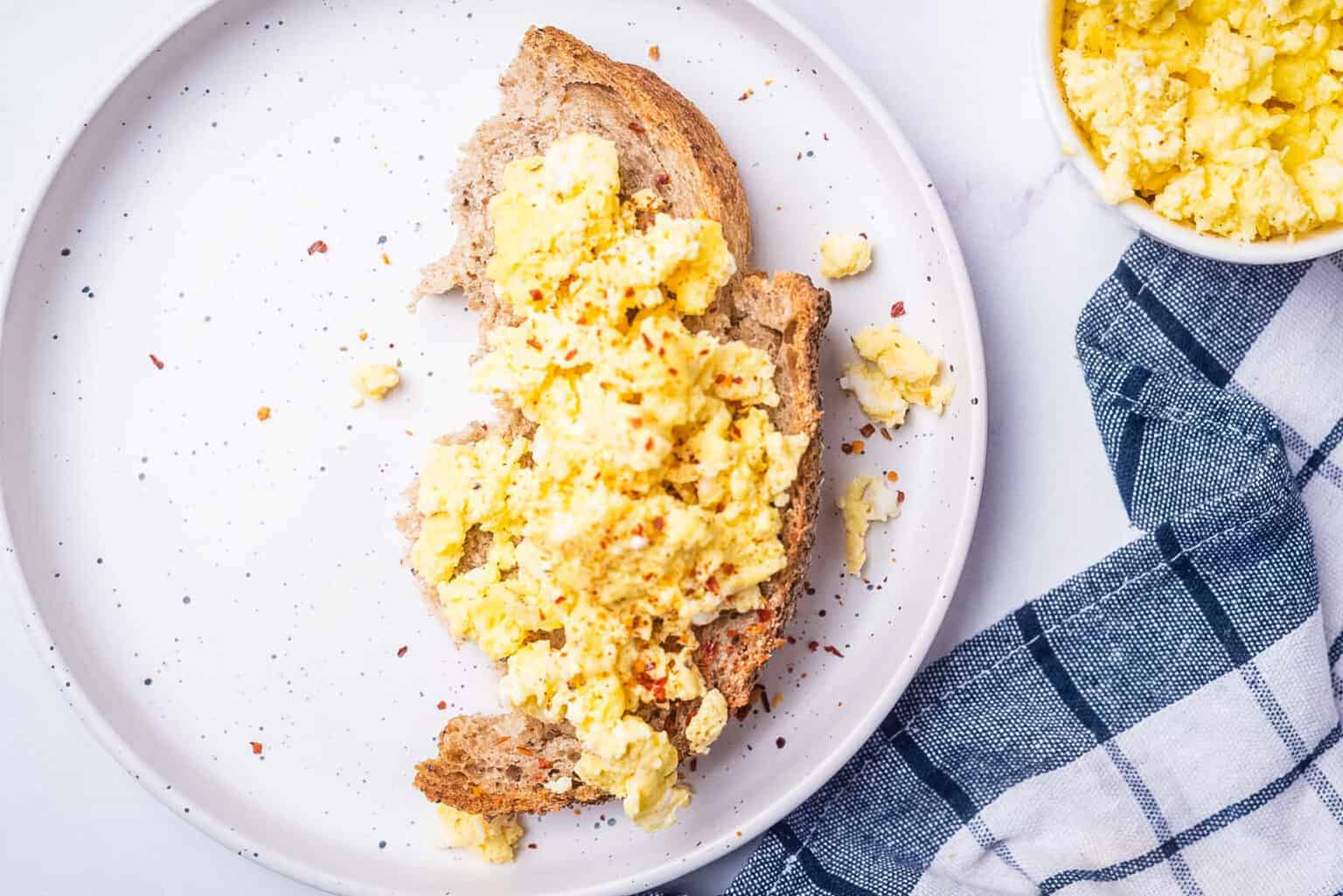 An overhead image of microwave scrambled eggs on a toast served on a plate.
