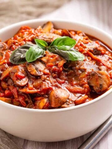 An image of mushroom ragu in a white bowl with a garnish of basil on top.