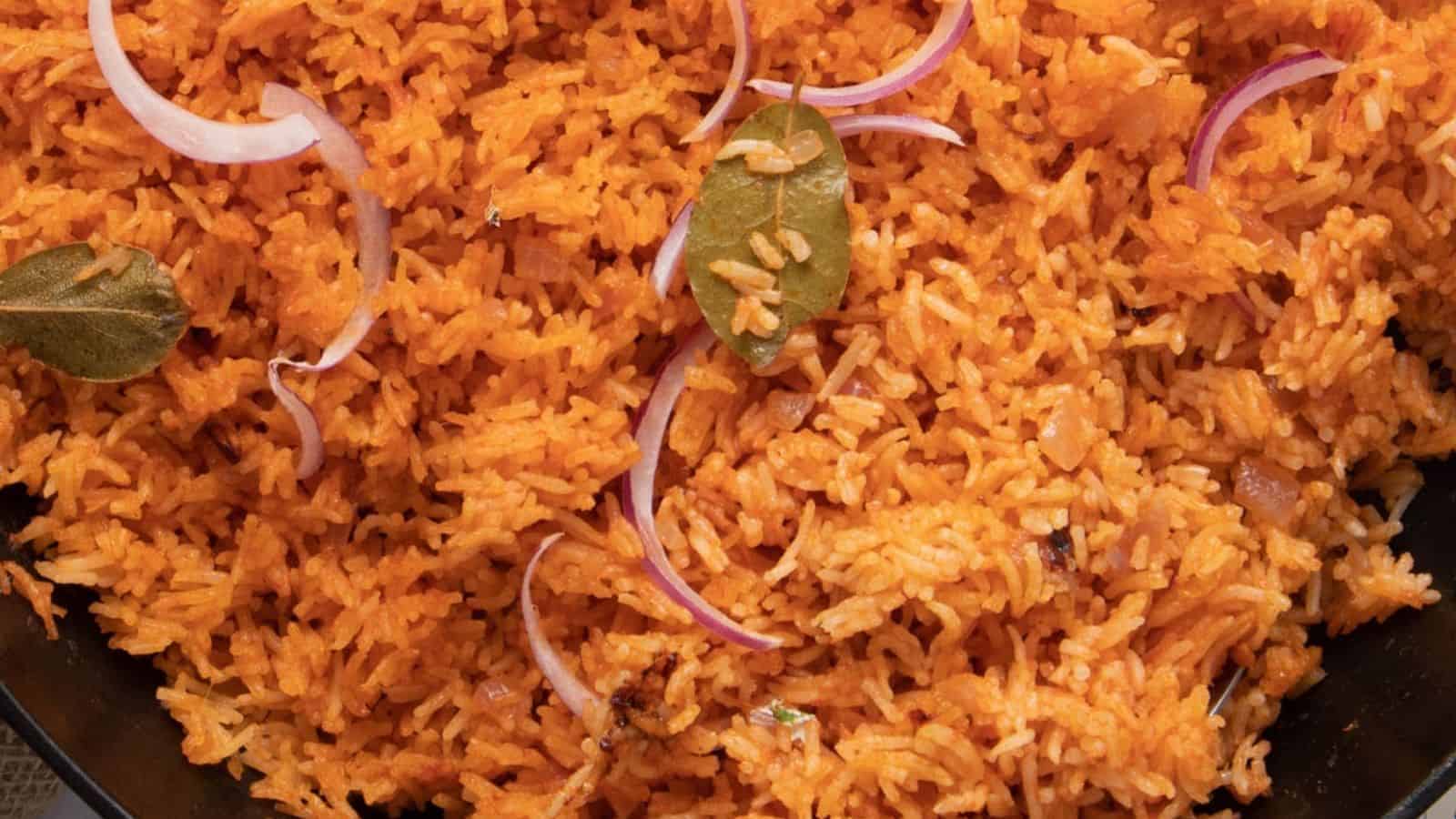 A close up image of nigerian jolloff rice garnished with slices of red onion and bay leaves.